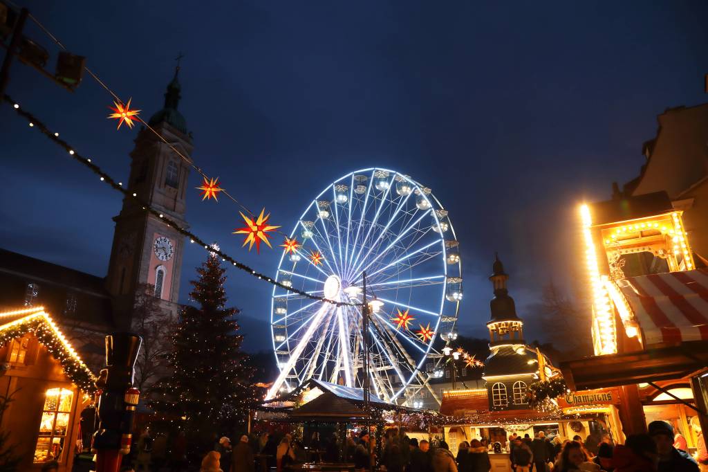 Beleuchtetes Riesenrad vor Kirchturm.