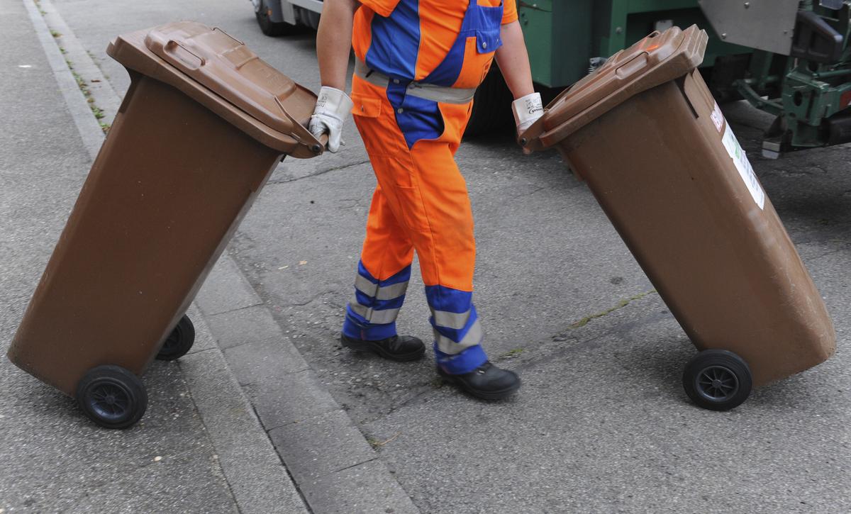 Ein Mitarbeiter der Abfallwirtschaft in ThÃ¼ringen schiebt zwei braune Tonnen mit BiomÃ¼ll zum MÃ¼llwagen (Symbolbild)